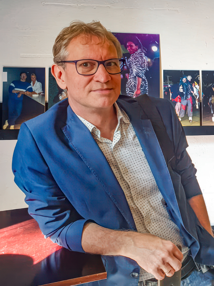 John, met op de achtergrond zijn honderden foto’s die hij maakte in de Bluetiek-in, tentoongesteld tijdens de expositie bij DIGIT-UP in 2020.